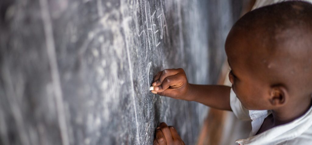 An African schoolchild draws on a blackboard with chalk